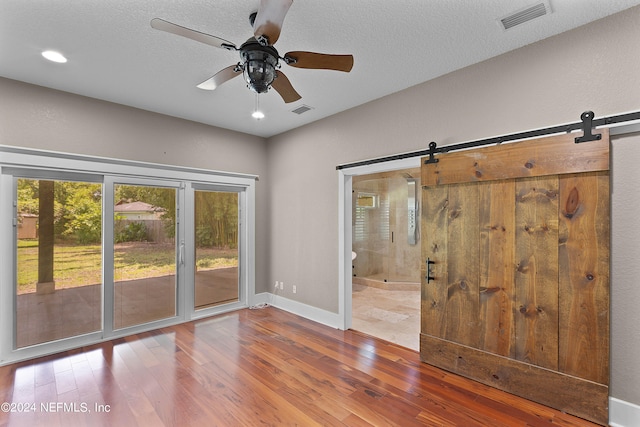 unfurnished room featuring ceiling fan, a barn door, hardwood / wood-style flooring, and a textured ceiling