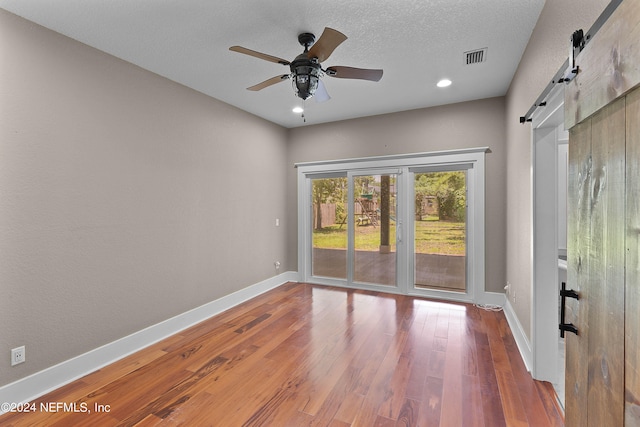 spare room with a barn door, a textured ceiling, ceiling fan, and hardwood / wood-style floors