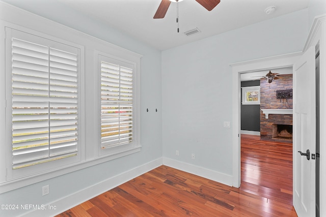 spare room featuring brick wall, ceiling fan, dark hardwood / wood-style floors, and a fireplace