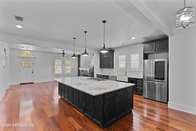 kitchen with a center island, dark hardwood / wood-style flooring, appliances with stainless steel finishes, a stone fireplace, and tasteful backsplash