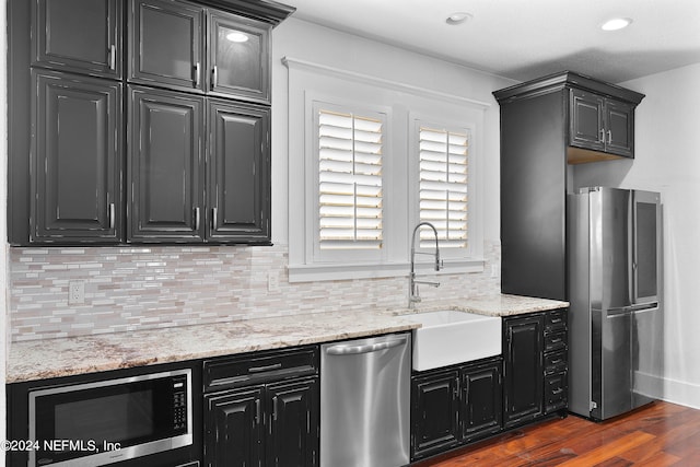 kitchen with light stone countertops, dark hardwood / wood-style flooring, stainless steel appliances, sink, and tasteful backsplash