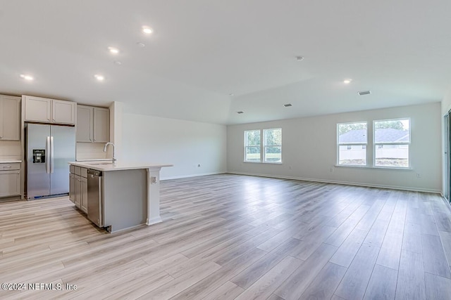 kitchen with appliances with stainless steel finishes, sink, a center island with sink, and light wood-type flooring