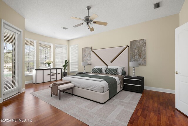 bedroom with baseboards, wood finished floors, visible vents, and a textured ceiling