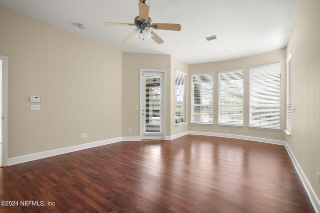 empty room with visible vents, baseboards, a textured ceiling, and dark wood-style floors