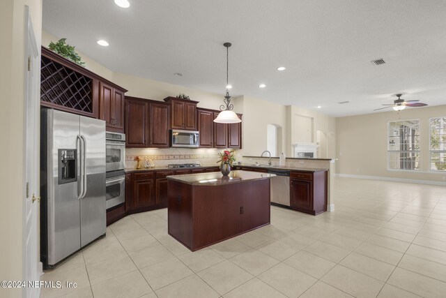 kitchen featuring backsplash, a kitchen island, a peninsula, stainless steel appliances, and a sink