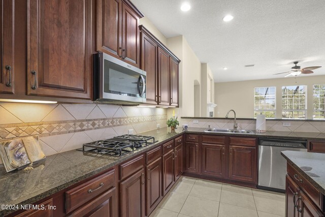 kitchen with a sink, stainless steel appliances, dark stone counters, light tile patterned flooring, and decorative backsplash