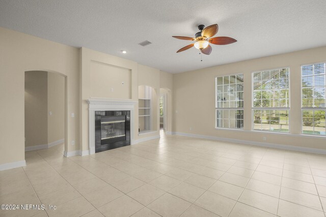 unfurnished living room with a glass covered fireplace, light tile patterned floors, arched walkways, and a textured ceiling