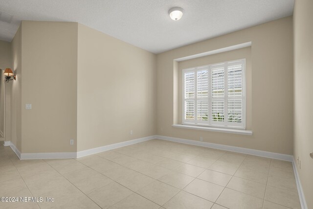 empty room featuring light tile patterned flooring, baseboards, and a textured ceiling