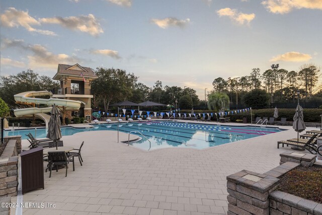 pool at dusk with a community pool, fence, a water slide, and a patio area