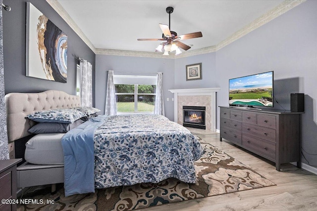 bedroom featuring crown molding, a tiled fireplace, a ceiling fan, wood finished floors, and baseboards