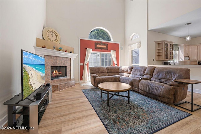 living room featuring light wood-style floors, a high ceiling, and a tile fireplace