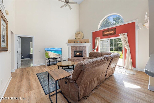 living area featuring baseboards, a ceiling fan, a tiled fireplace, a towering ceiling, and light wood-style floors