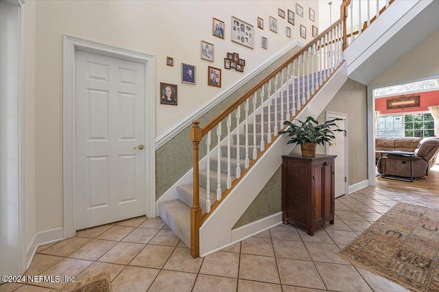 stairway featuring tile patterned flooring, a towering ceiling, and baseboards