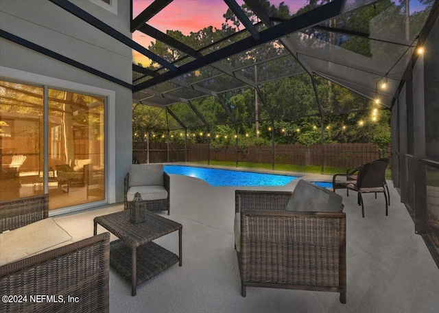 pool at dusk featuring glass enclosure and a patio