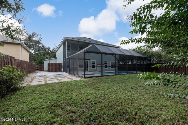 rear view of house with glass enclosure, a fenced in pool, a yard, and a patio