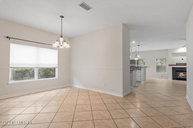 tiled empty room with a textured ceiling, a wealth of natural light, and a notable chandelier