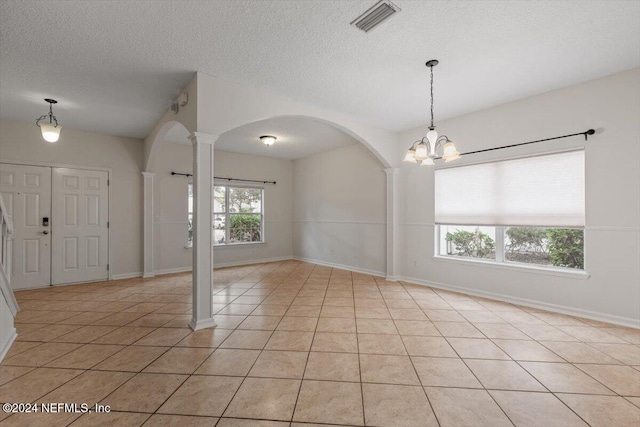 spare room featuring a notable chandelier, light tile patterned floors, a textured ceiling, and ornate columns