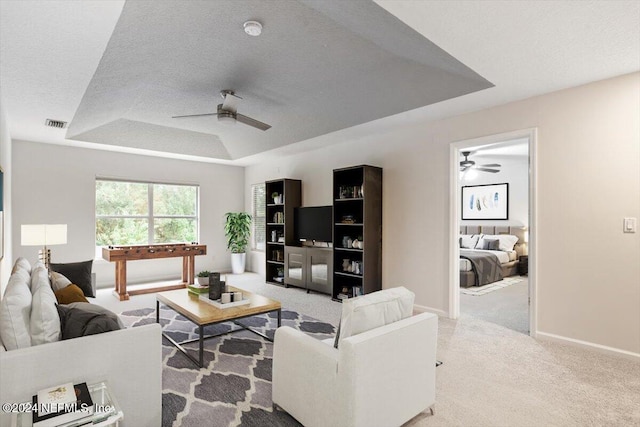 carpeted living room with ceiling fan, a raised ceiling, and a textured ceiling