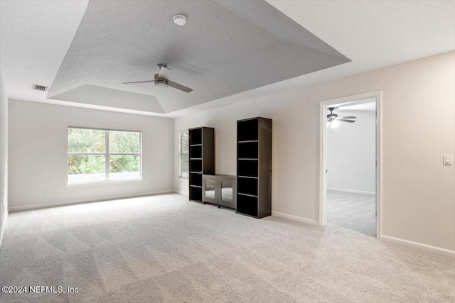 interior space featuring a raised ceiling, ceiling fan, light colored carpet, and a textured ceiling