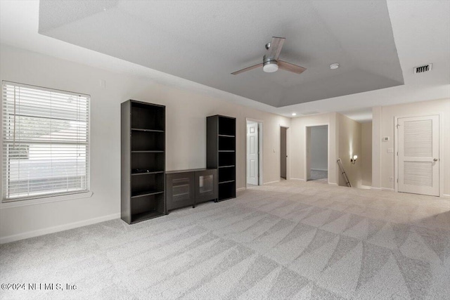 unfurnished living room featuring ceiling fan, light colored carpet, and a tray ceiling