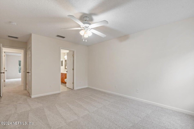 unfurnished bedroom with a textured ceiling, ceiling fan, light carpet, and ensuite bath