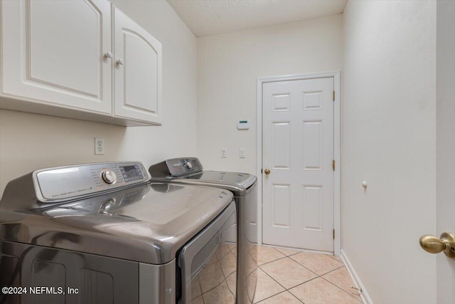 clothes washing area with cabinets, washer and clothes dryer, and light tile patterned flooring