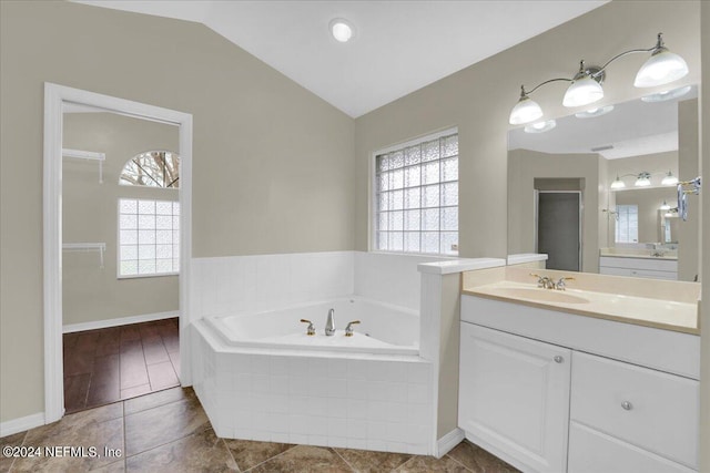 bathroom featuring lofted ceiling, tiled tub, vanity with extensive cabinet space, and a healthy amount of sunlight