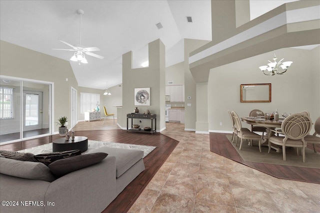 tiled living room with high vaulted ceiling and ceiling fan with notable chandelier