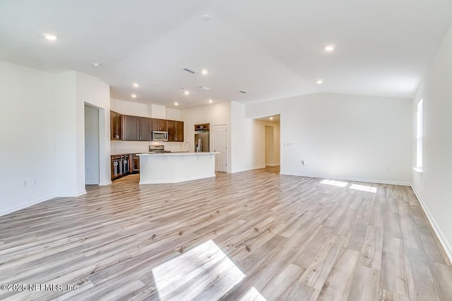 unfurnished living room with vaulted ceiling, light hardwood / wood-style flooring, and sink