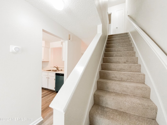 staircase with a textured ceiling, sink, and light hardwood / wood-style flooring