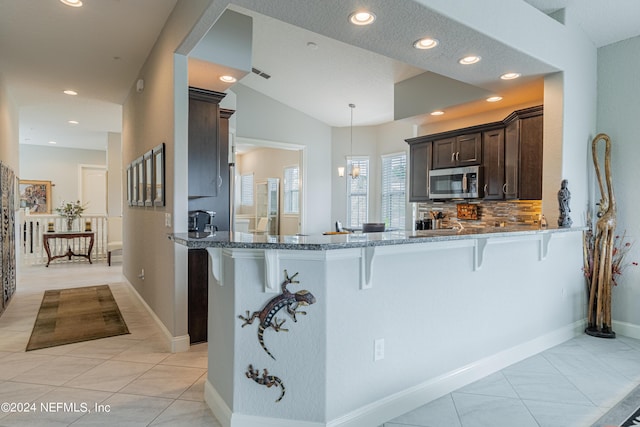 kitchen featuring hanging light fixtures, a kitchen breakfast bar, dark brown cabinetry, light tile patterned flooring, and kitchen peninsula