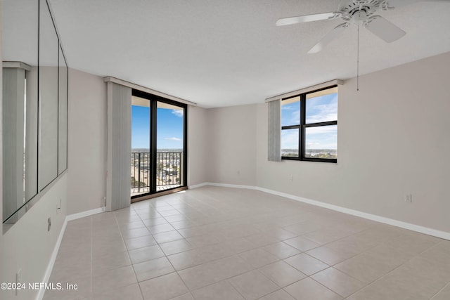 spare room featuring a textured ceiling, floor to ceiling windows, light tile patterned floors, and ceiling fan