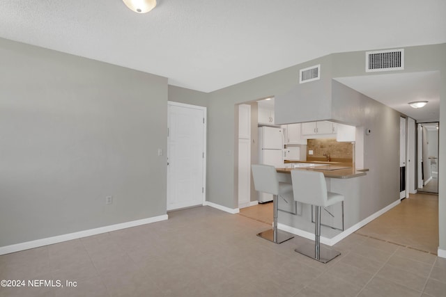 kitchen featuring backsplash, a breakfast bar, kitchen peninsula, white refrigerator, and white cabinets