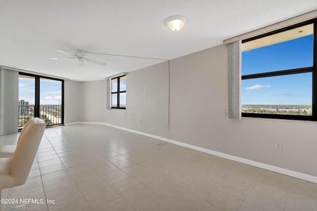 tiled empty room with ceiling fan, a wealth of natural light, and expansive windows