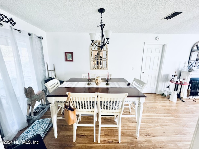 dining room with light wood-type flooring, a textured ceiling, and a chandelier