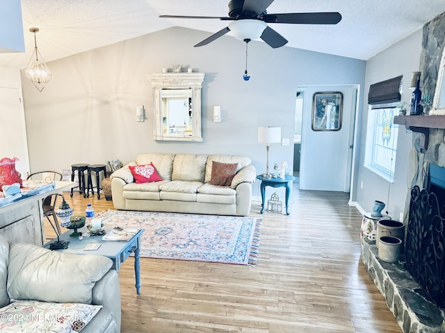 living room with ceiling fan, light hardwood / wood-style floors, a stone fireplace, and lofted ceiling