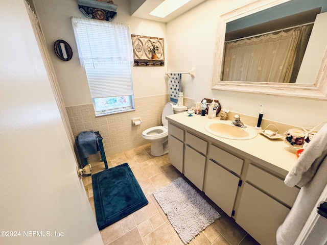 bathroom with tile walls, toilet, vanity, and tile patterned floors