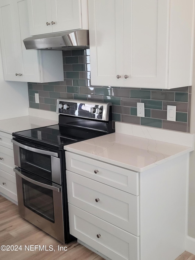 kitchen with light stone counters, light hardwood / wood-style flooring, backsplash, wall chimney range hood, and range with two ovens