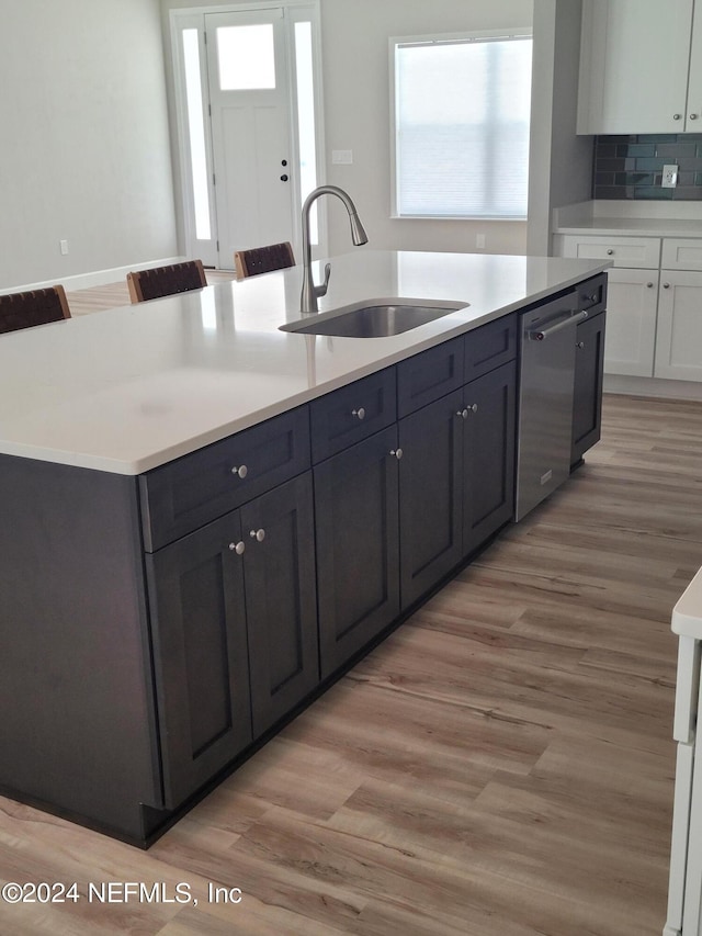 kitchen featuring light wood-type flooring, a center island with sink, white cabinetry, dishwasher, and sink