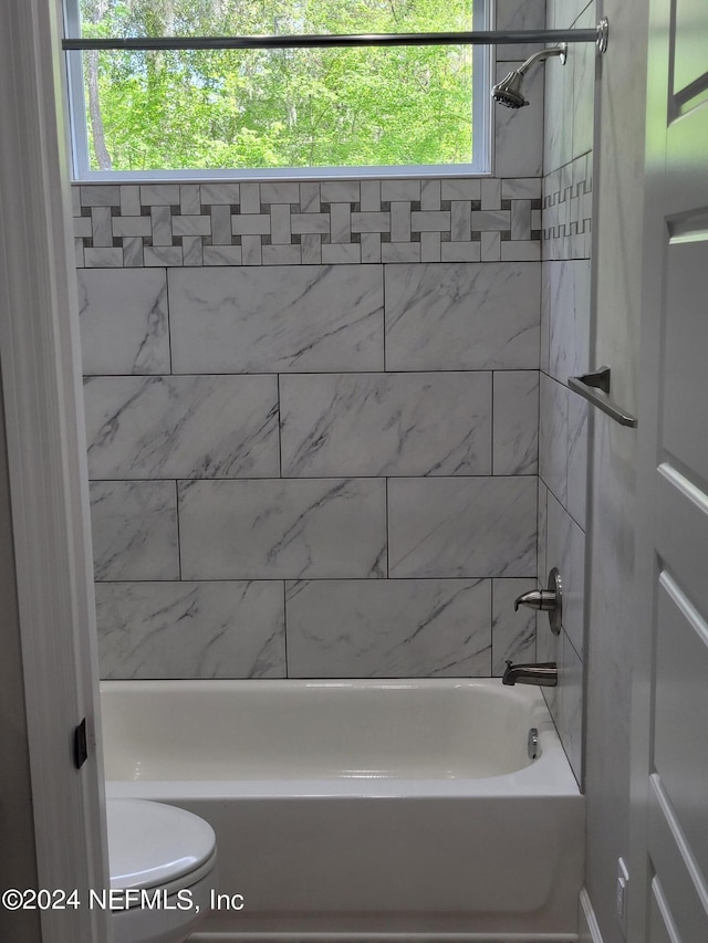 bathroom featuring a wealth of natural light, toilet, and tiled shower / bath