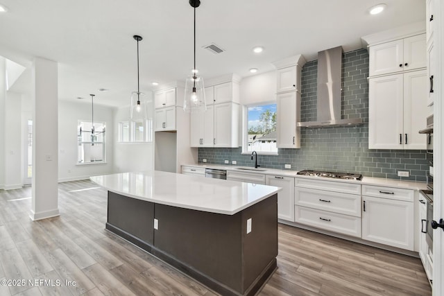 kitchen with sink, a center island, white cabinets, decorative light fixtures, and wall chimney exhaust hood