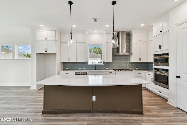 kitchen with wall chimney range hood, sink, white cabinets, and a kitchen island