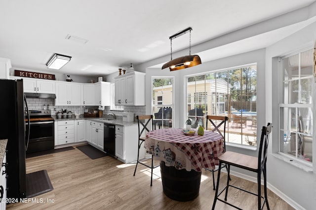 kitchen featuring pendant lighting, light hardwood / wood-style floors, black appliances, white cabinetry, and light stone counters