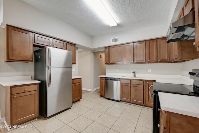 kitchen with sink, stainless steel appliances, light tile floors, a textured ceiling, and wall chimney range hood