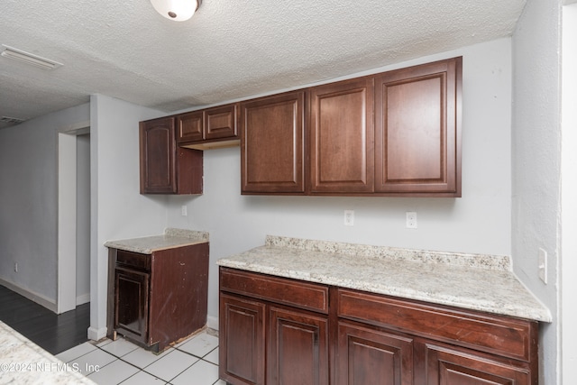 kitchen featuring light tile floors, a textured ceiling, dark brown cabinets, and light stone counters