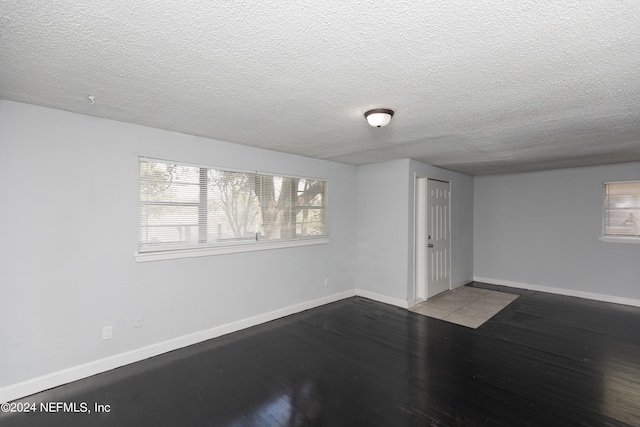 empty room featuring plenty of natural light, a textured ceiling, and dark hardwood / wood-style flooring