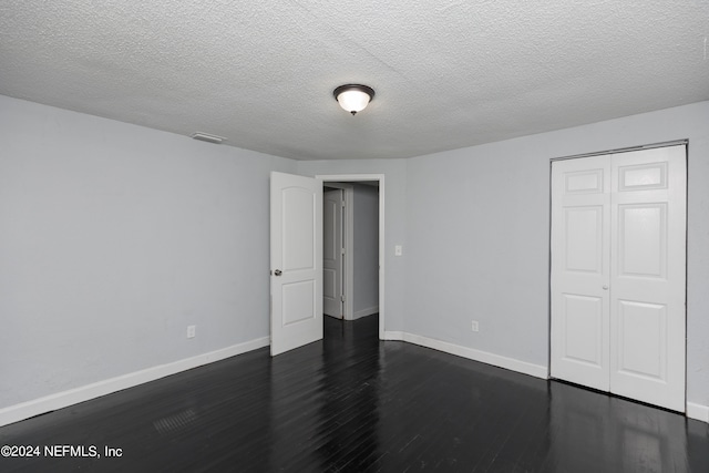 unfurnished bedroom with a textured ceiling, a closet, and dark hardwood / wood-style floors