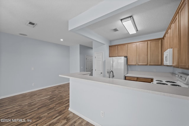 kitchen with a textured ceiling, kitchen peninsula, white appliances, and hardwood / wood-style flooring