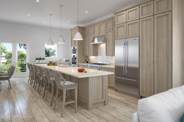 kitchen featuring hanging light fixtures, a kitchen island with sink, light hardwood / wood-style flooring, tasteful backsplash, and high quality appliances