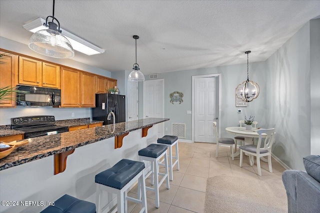 kitchen featuring hanging light fixtures, black appliances, a kitchen breakfast bar, a notable chandelier, and light tile floors